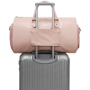 Pink duffel bag on top of a silver suitcase with a white background