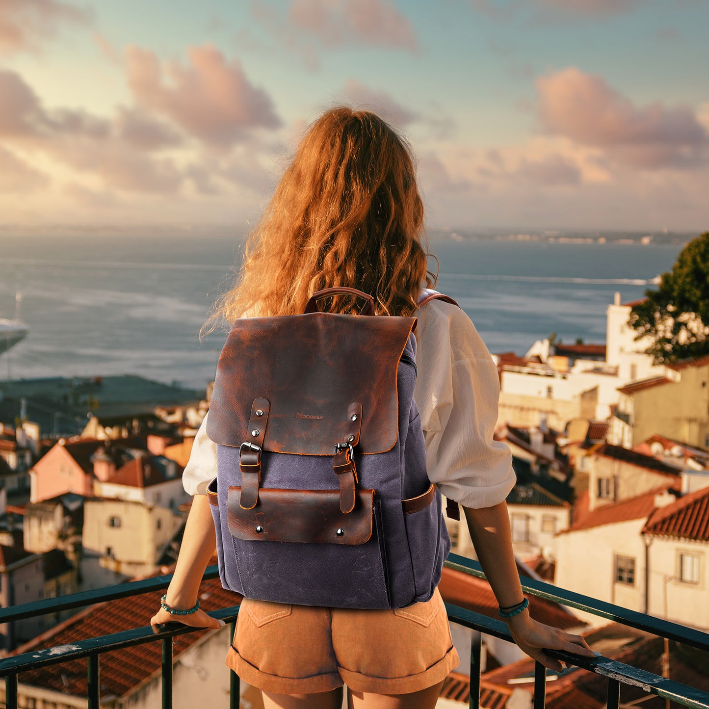 Person with a backpack overlooking a coastal town at sunset