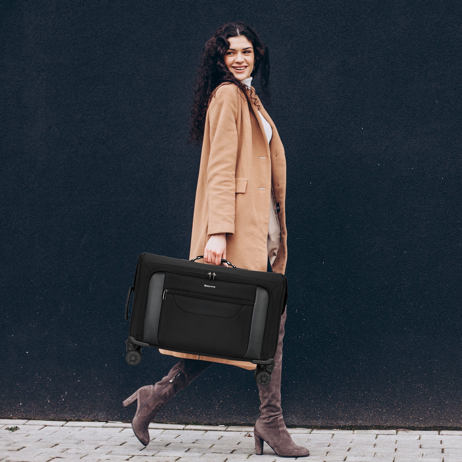 Woman in a tan coat holding a black suitcase against a dark background