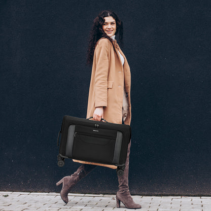 Woman in a tan coat holding a black suitcase against a dark background
